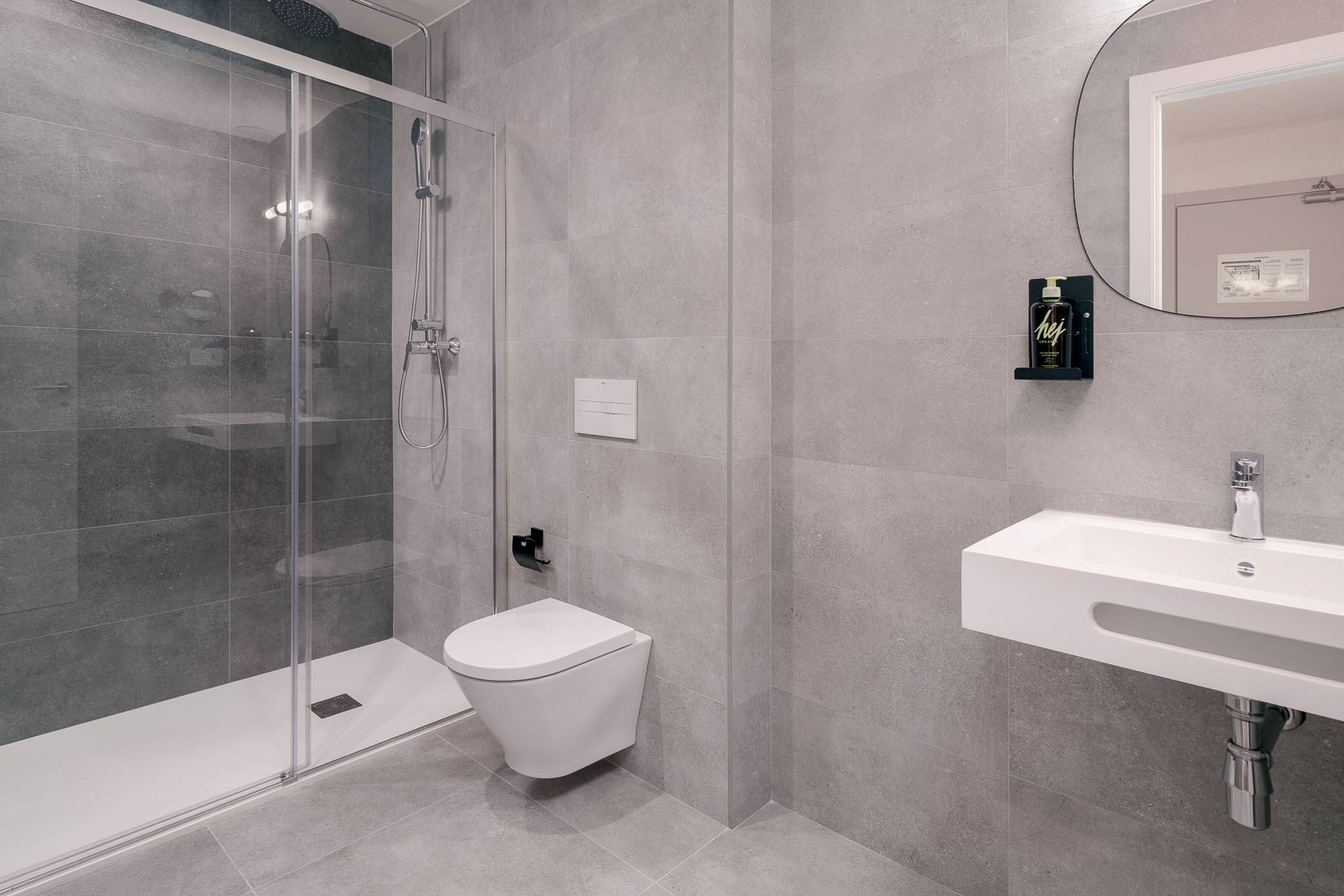 A modern bathroom with a glass-enclosed shower, a white toilet, and a white sink with a mirror above it.