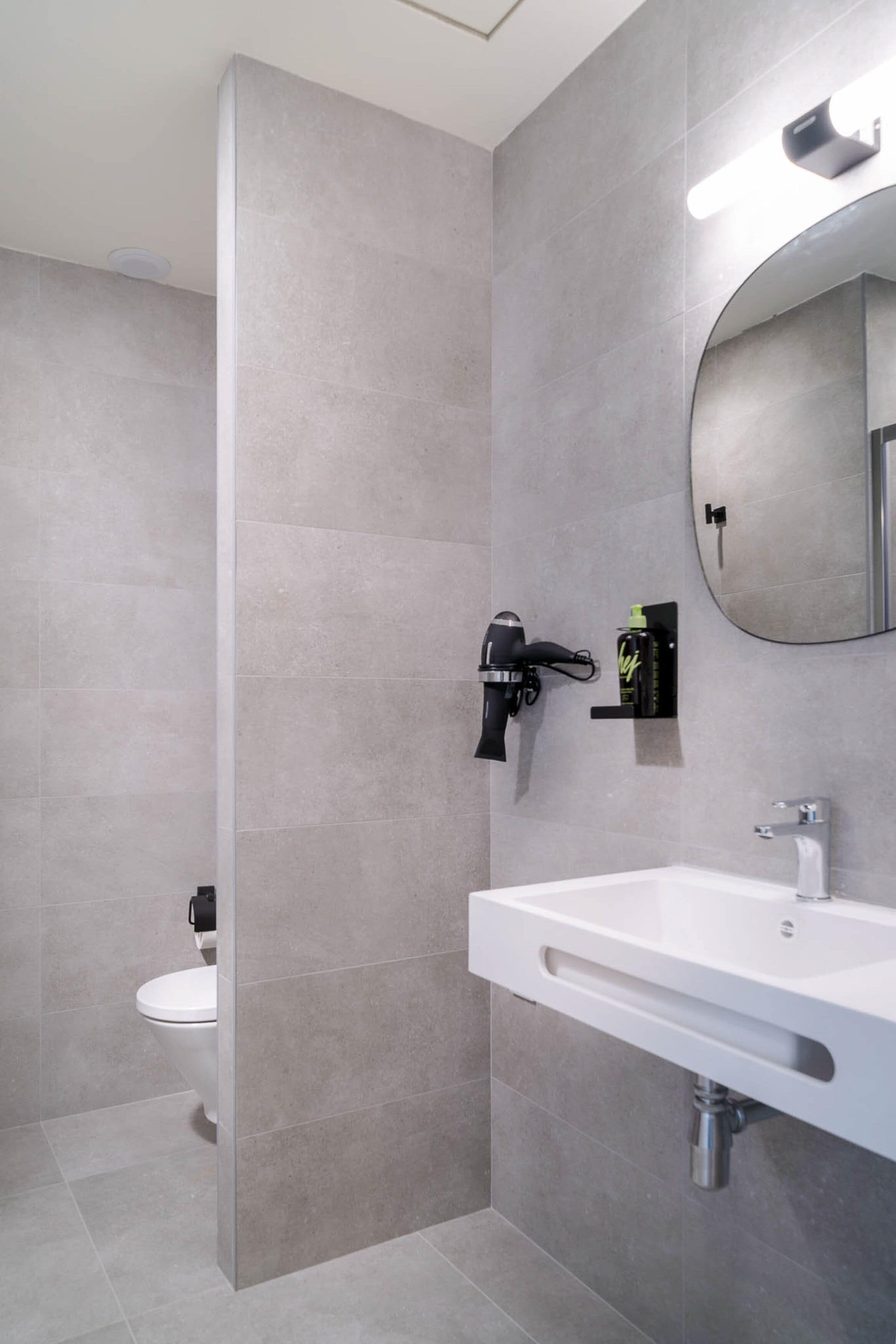 A modern bathroom with a white sink, a mirror, and a hairdryer mounted on the wall.