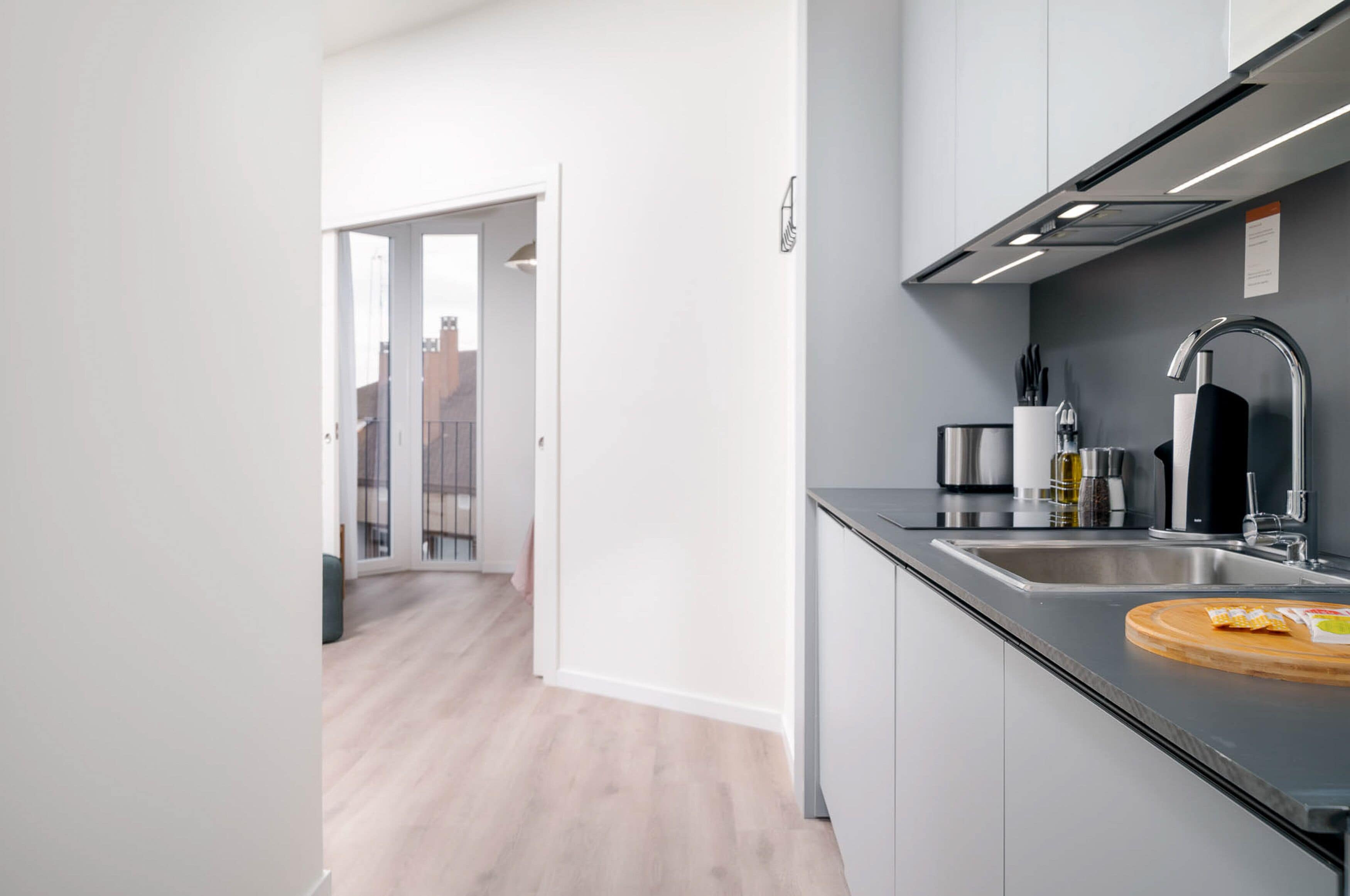 Une cuisine moderne dotée d’un évier en acier inoxydable, d’une planche à découper et offrant une vue sur la ville grâce à une porte vitrée.