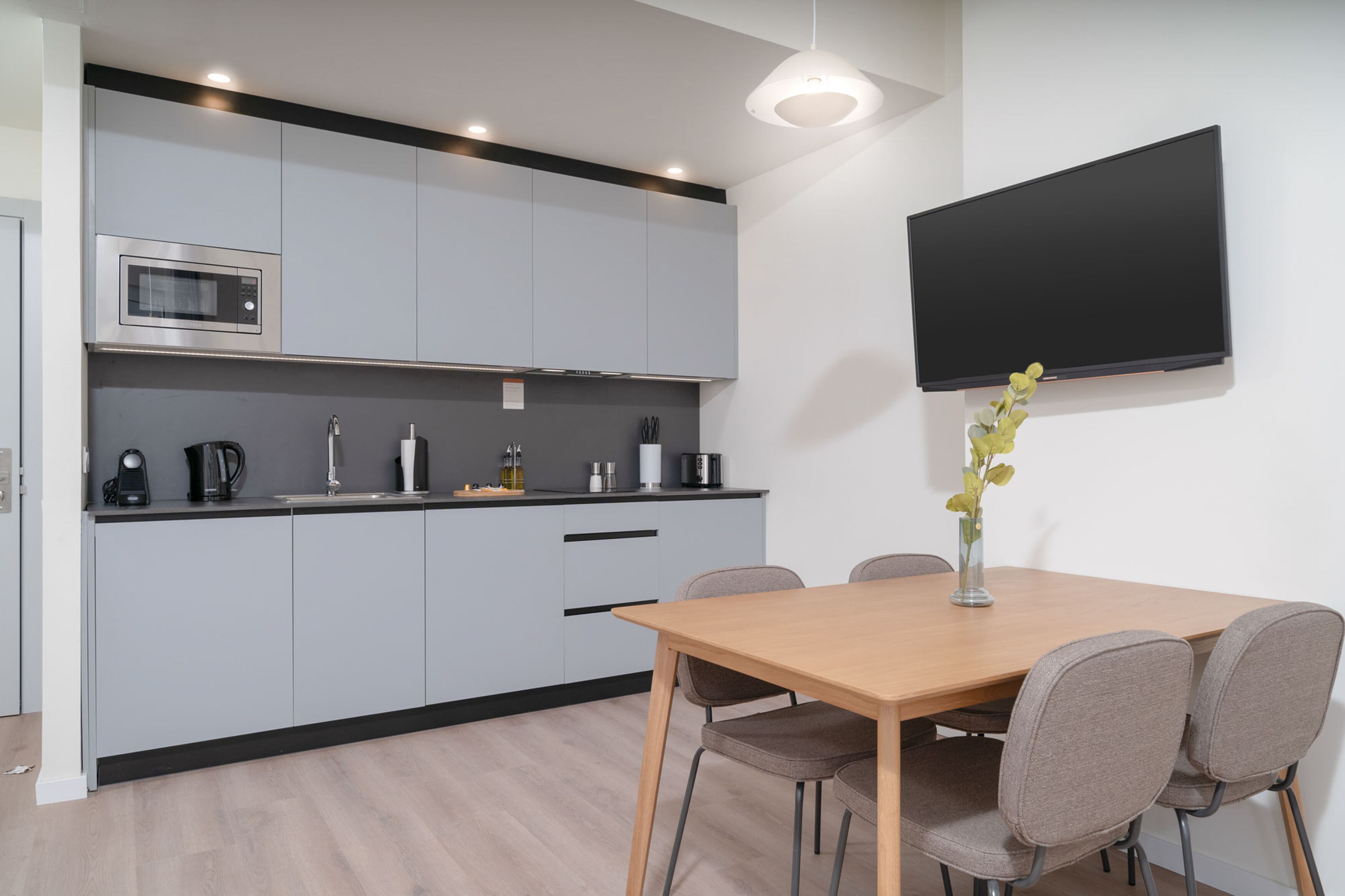 A modern kitchen with grey cabinets, a microwave, and a flat-screen TV mounted on the wall.