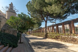 Un sendero pavimentado bordeado de árboles y una estatua, que conduce a un edificio de fachada de ladrillo.