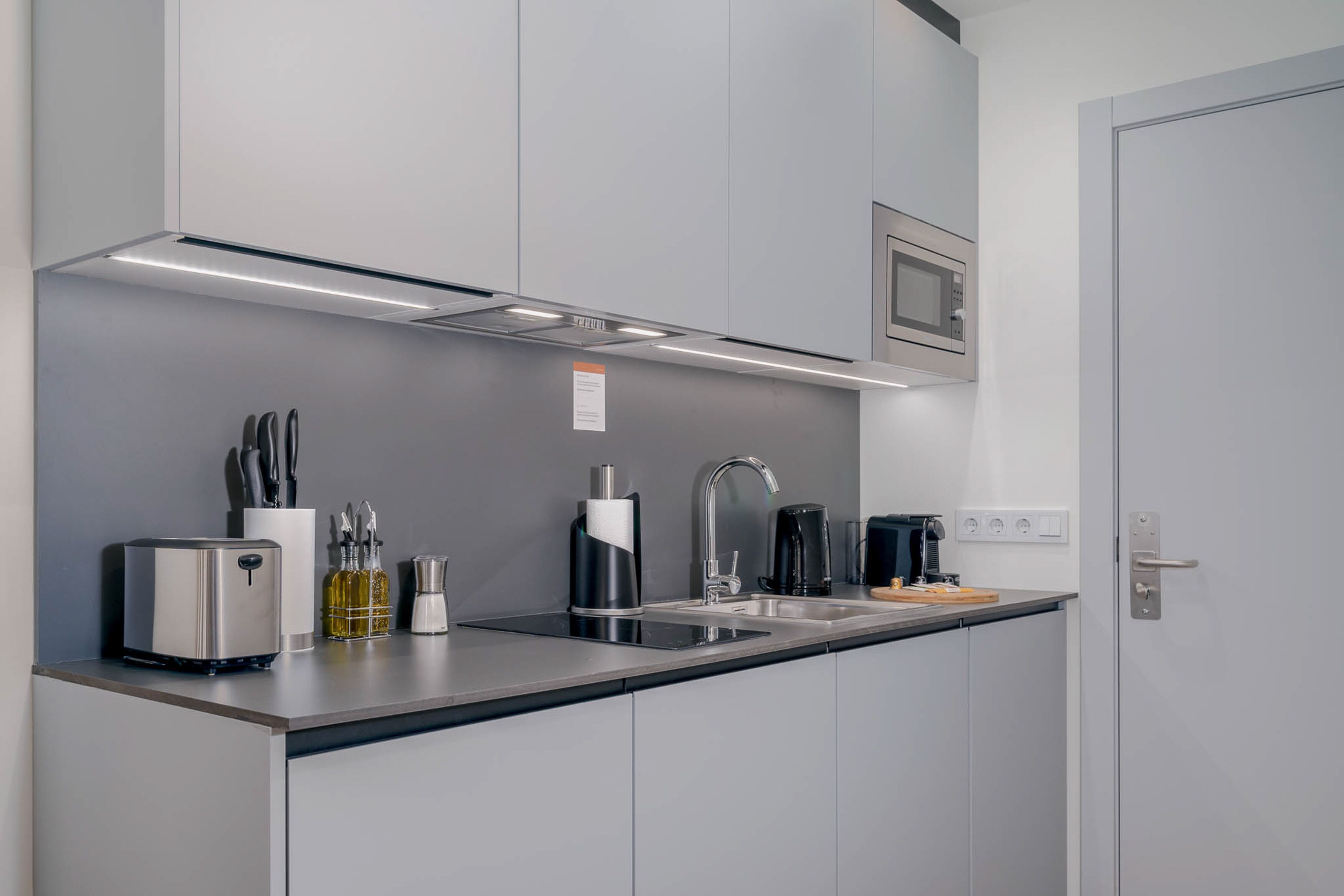 Una cocina moderna con encimera de acero inoxidable, microondas integrado, cafetera y tostadora.