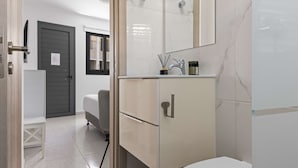 A modern bathroom with a white toilet, a beige vanity with a mirror, and a shower area. - Phaedrus Living: Alkminis Seaside Suites Sand (Paphos)