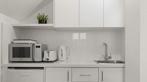 A modern kitchen with white cabinets, a microwave, toaster, coffee maker, and a dishwasher. - Phaedrus Living: Alkminis Seaside Suites Sand (Paphos)