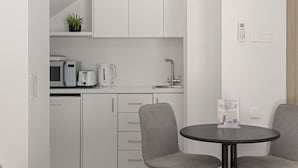 A modern kitchen with white cabinets, a microwave, toaster, and coffee maker. There is a small table with two chairs and a sign on it. - Phaedrus Living: Alkminis Seaside Suites Sand (Paphos)