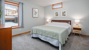 A bedroom with a bed, bedside lamps, a window with curtains, and wall art. - Pet-friendly home with fenced-in yard and hot tub (Grawn)