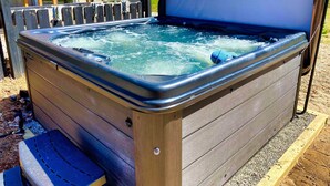 A hot tub with a wooden deck and a metal frame, situated outdoors. - Pet-friendly home with fenced-in yard and hot tub (Grawn)