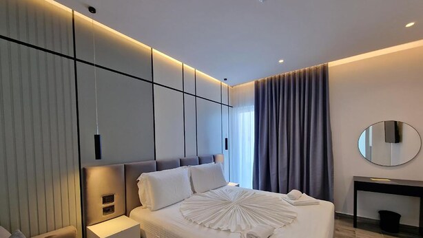 Una habitación de hotel moderna con una cama grande, una mesita de noche, un espejo y una ventana con cortinas.
