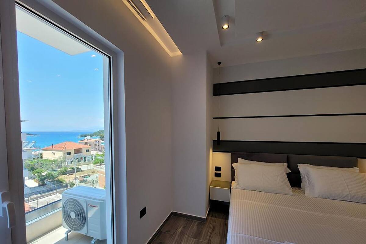 A modern bedroom with a large bed, a view of the sea, and a balcony with an air conditioning unit.