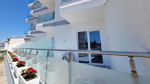 Un edificio moderno de varios pisos con balcones, barandilla de vidrio y macetas con flores.