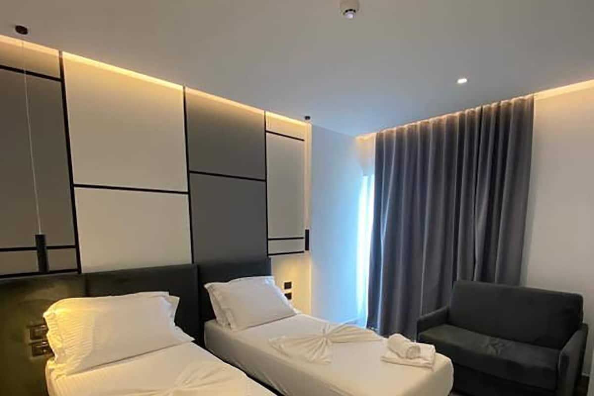 A hotel room with two beds, a sofa, and a large window with curtains.
