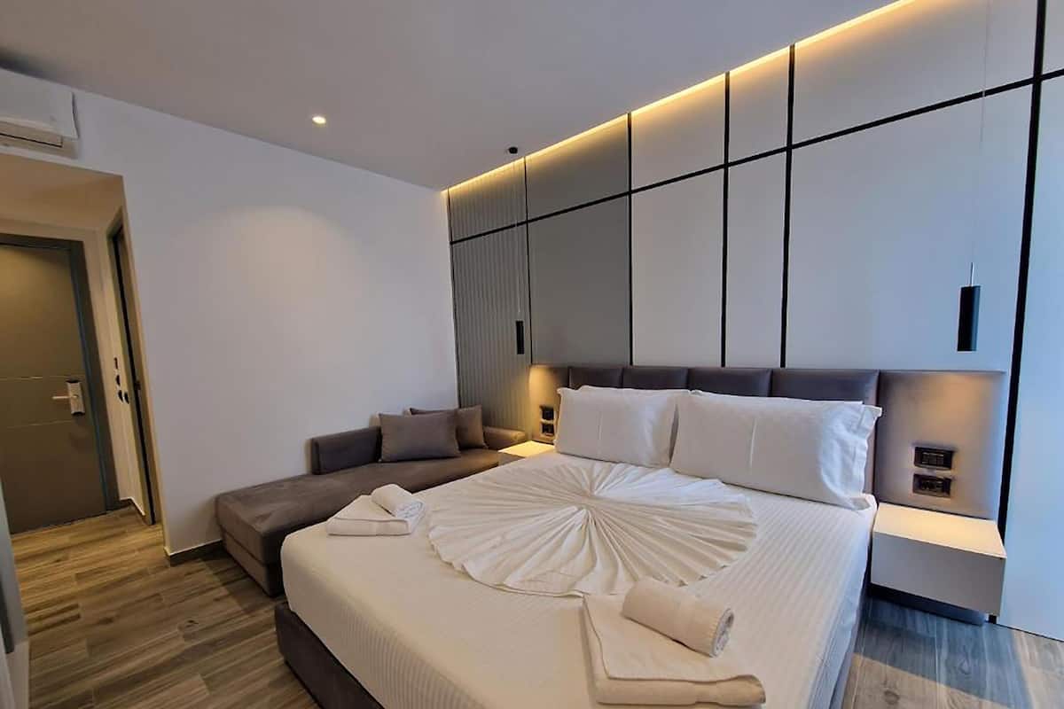 A modern hotel room with a large bed, a sofa, and a built-in wardrobe.