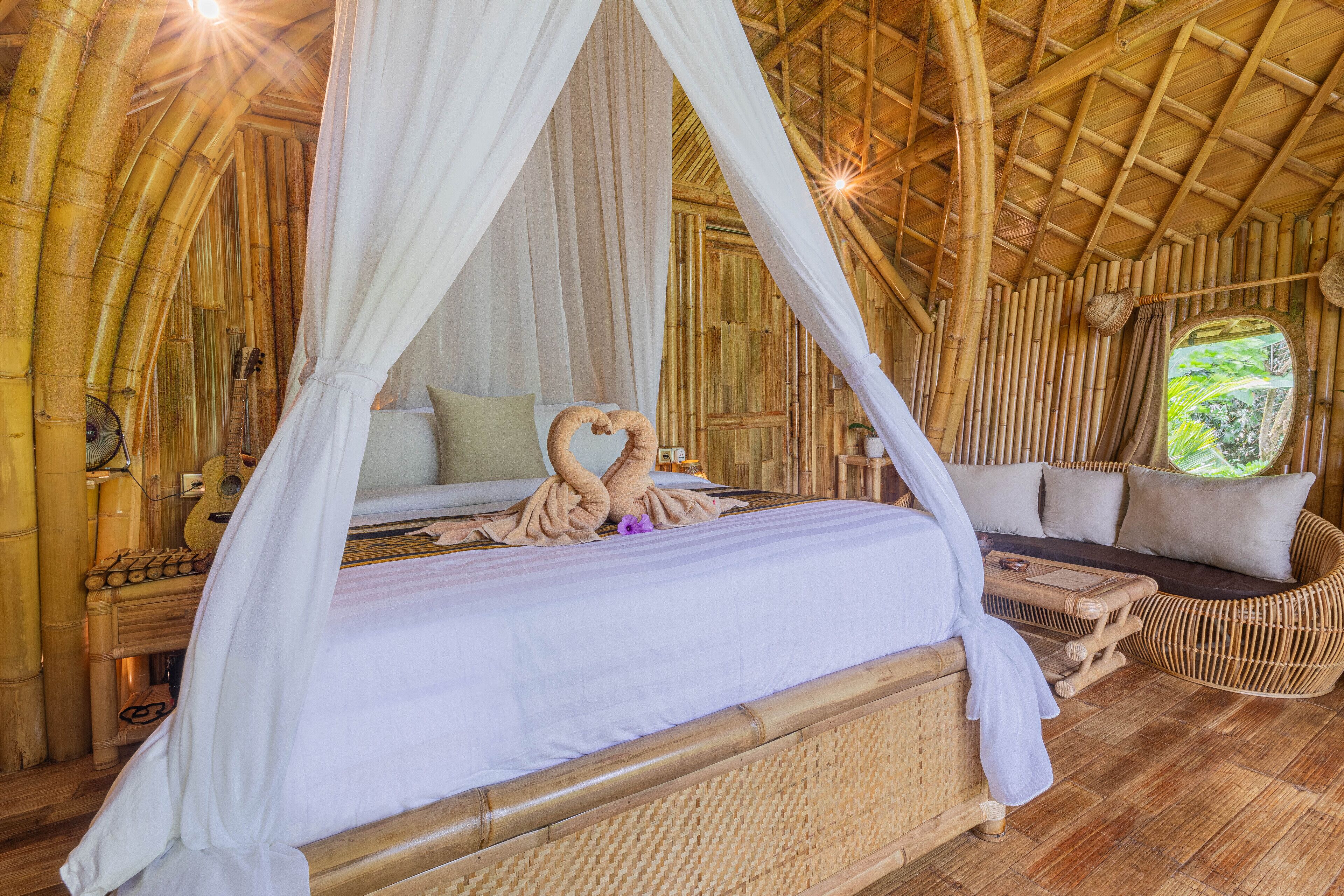Quarto com cama sob dossel, sofá e janela com vista para área verde.
