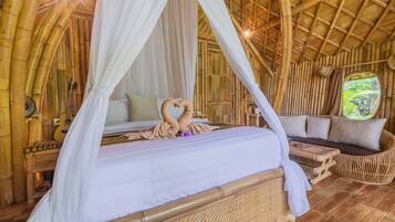 Quarto com cama sob dossel, sofá e janela com vista para área verde.