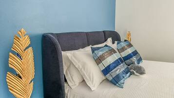 Ein Bett mit dunklem Kopfteil, weißen und blauen Streifenpillows sowie ein dekoratives goldenes Blatt auf einem schwarzen Beistelltisch.