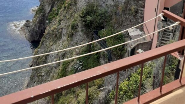 Un bâtiment situé sur la côte, adossé à une falaise rocheuse, doté d’un balcon avec une balustrade et offrant une vue sur la mer.