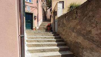 A narrow stone staircase leading up to a building with a pink facade and a beige wall.