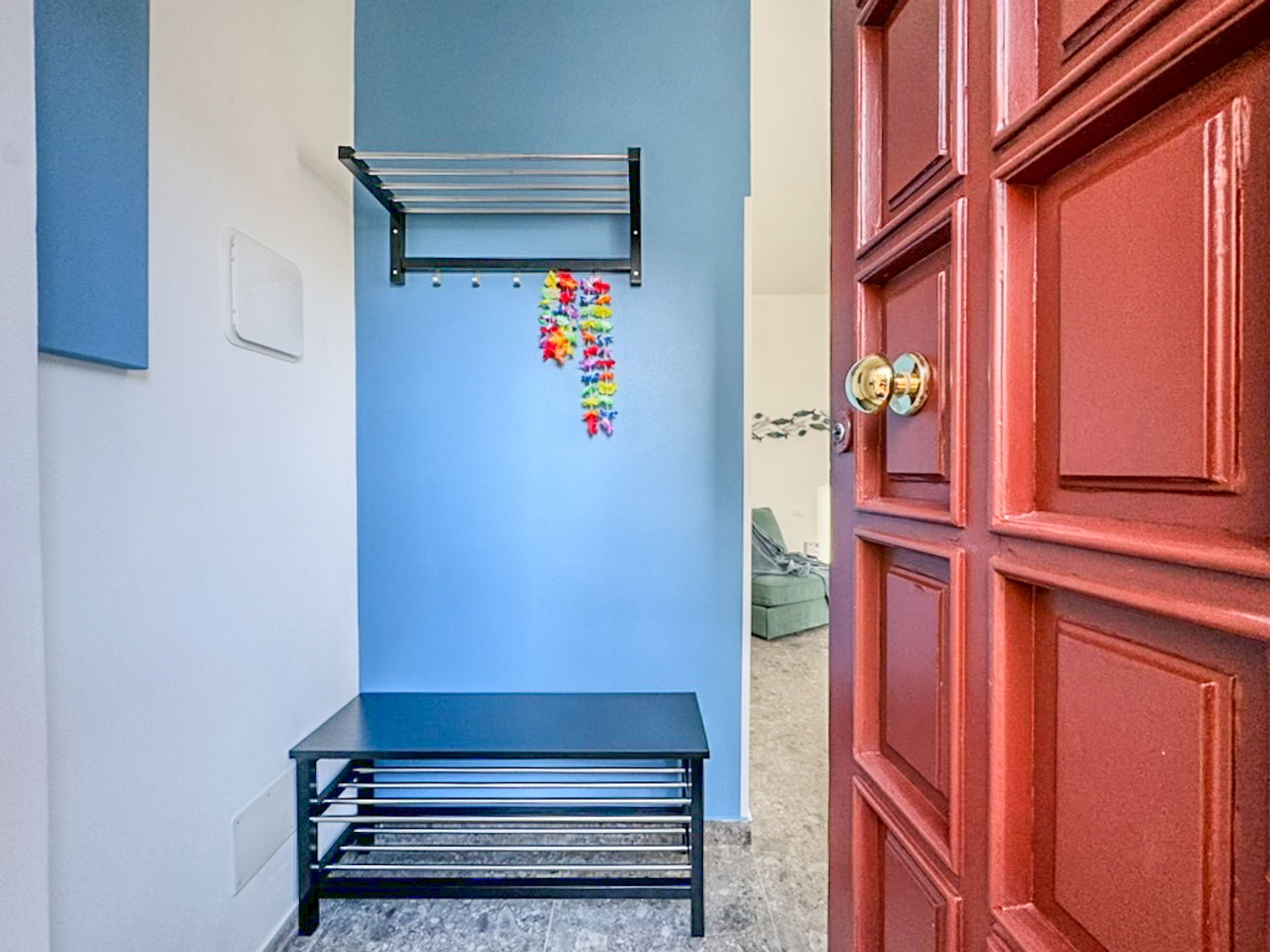 A hallway with a blue wall, a black bench, a metal rack, and a red door.