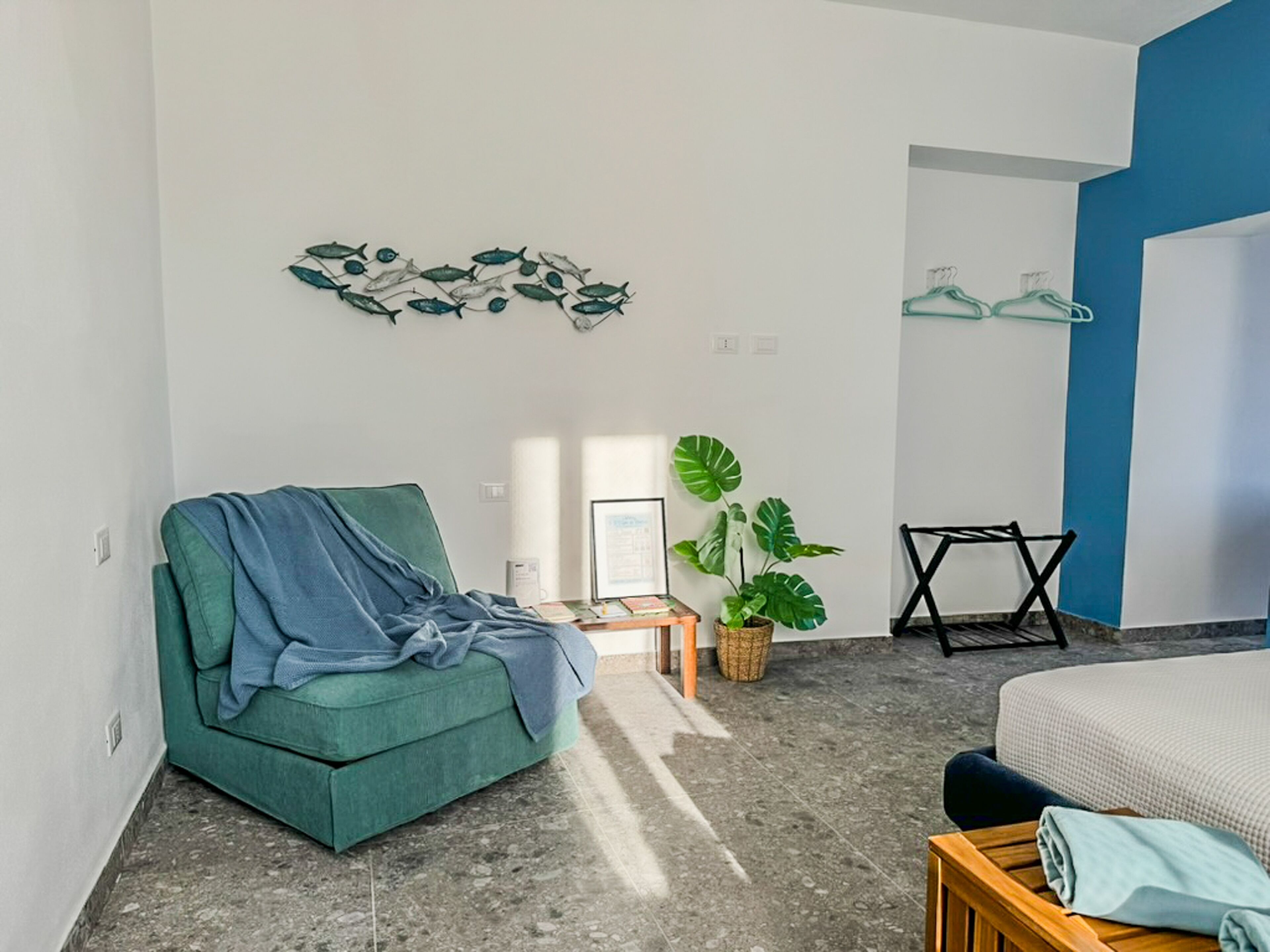 A modern bedroom with a green sofa, a bed with a white cover, a plant, and a wall art piece.