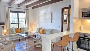 A modern living room with a sofa, coffee table, and bar stools. There is a kitchen area with a stove and microwave. - Cosy villa with private swimming pool, magnificent views, for 6 PAX (Tarifa)