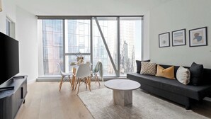 A modern living room with a large window, a sofa, a coffee table, and a TV.