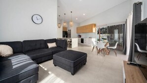 A modern living room with a dark sofa, a small ottoman, and a dining area with white chairs. - Oceanfront View Beachside Bliss – Ocean Views, Plunge Pool & Pet Friendly (Sapphire Beach)