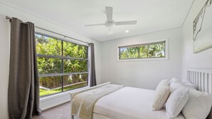 A bedroom with a bed, two windows, a ceiling fan, and a view of greenery outside. - Oceanfront View Beachside Bliss – Ocean Views, Plunge Pool & Pet Friendly (Sapphire Beach)