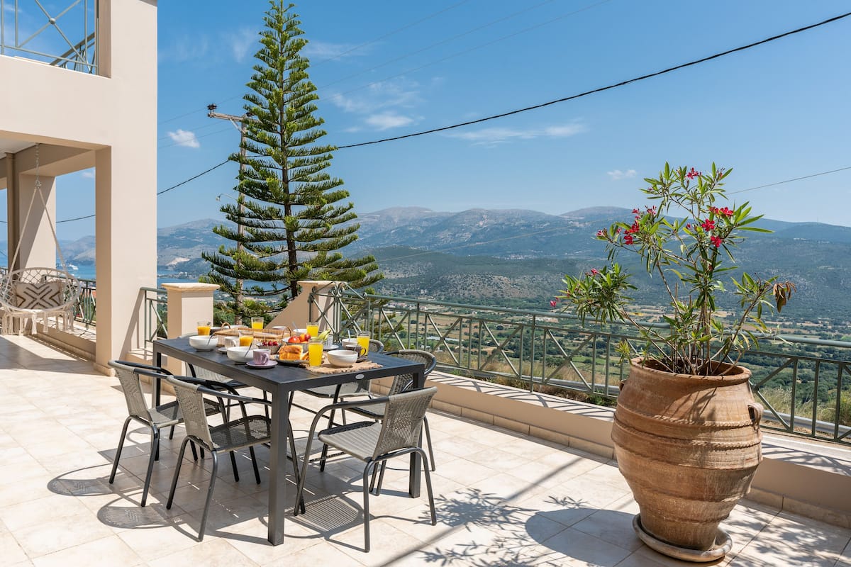 Une terrasse avec une table dressée pour le petit-déjeuner, une plante en pot et une vue sur les montagnes.