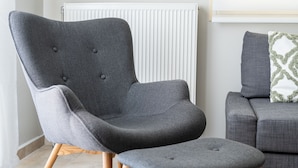 A modern living room with a grey armchair and ottoman, wooden floor, and a grey sofa with a patterned pillow. - Horizon Apartment (Kefalonia)