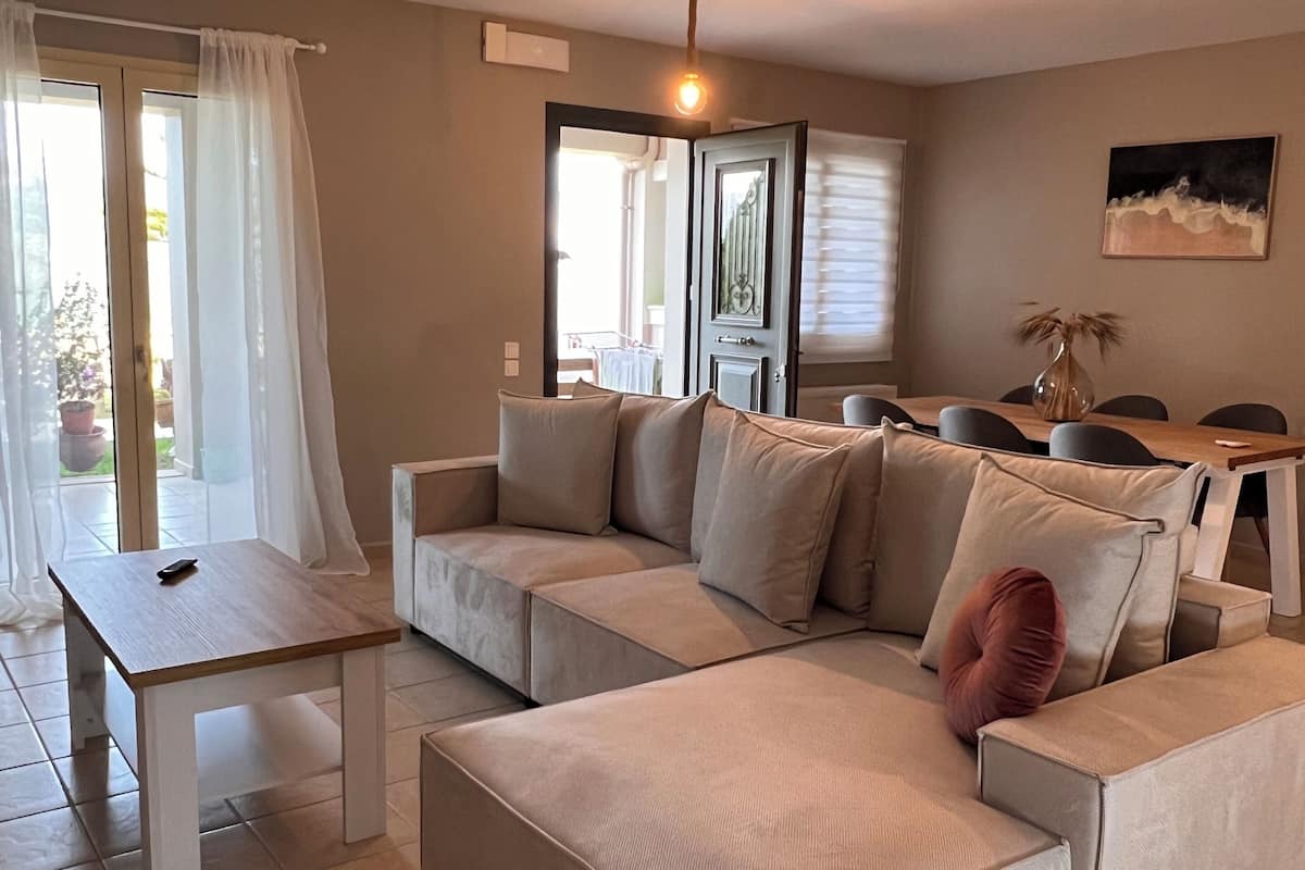 Un salon moderne avec un canapé d’angle beige, une table basse en bois et une table à manger.