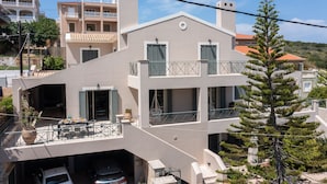 A modern two-story building with a balcony, outdoor seating area, and a garage. - Horizon Apartment (Kefalonia)