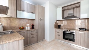 A modern kitchen with light wood cabinetry, granite countertops, a built-in oven, and a stainless steel range hood. - Horizon Apartment (Kefalonia)