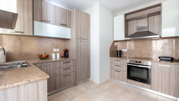 A modern kitchen with light wood cabinetry, granite countertops, a built-in oven, and a stainless steel range hood.