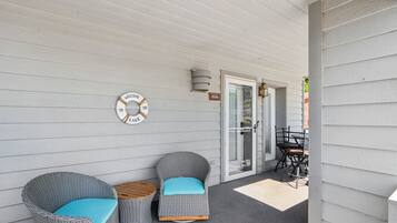 A covered porch with wicker furniture, a welcome sign, and a door with a glass panel.