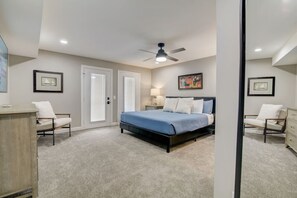 A bedroom with a bed, two chairs, a dresser, a ceiling fan, and framed artwork on the walls.