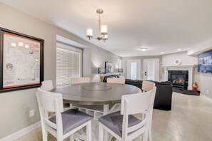 A modern living room with a round dining table, white chairs, a fireplace, and a mounted TV.