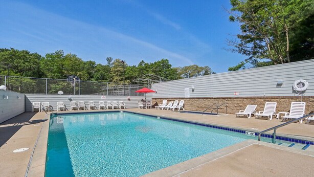 A swimming pool with clear blue water, surrounded by white lounge chairs and a red umbrella. - Some'R on the Beach - Beachfront Condo for Six (Wisconsin Dells)