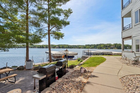 A lakeside patio with outdoor grills, picnic tables, and umbrellas.