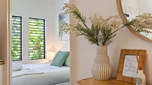 A bedroom with a bed, a bedside table with a vase of flowers, a framed picture, and a mirror.