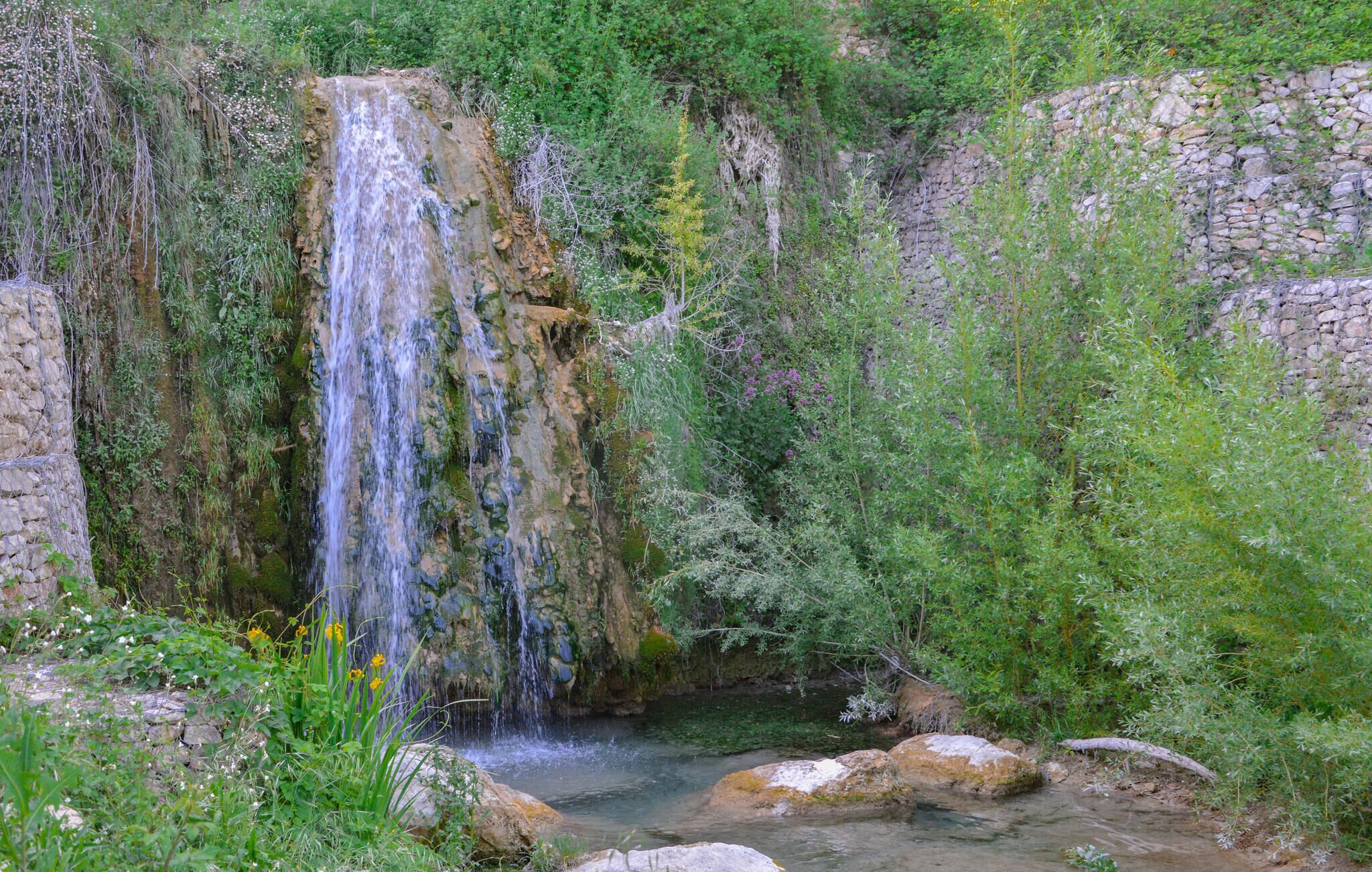 A natural waterfall surrounded by greenery and rocks.