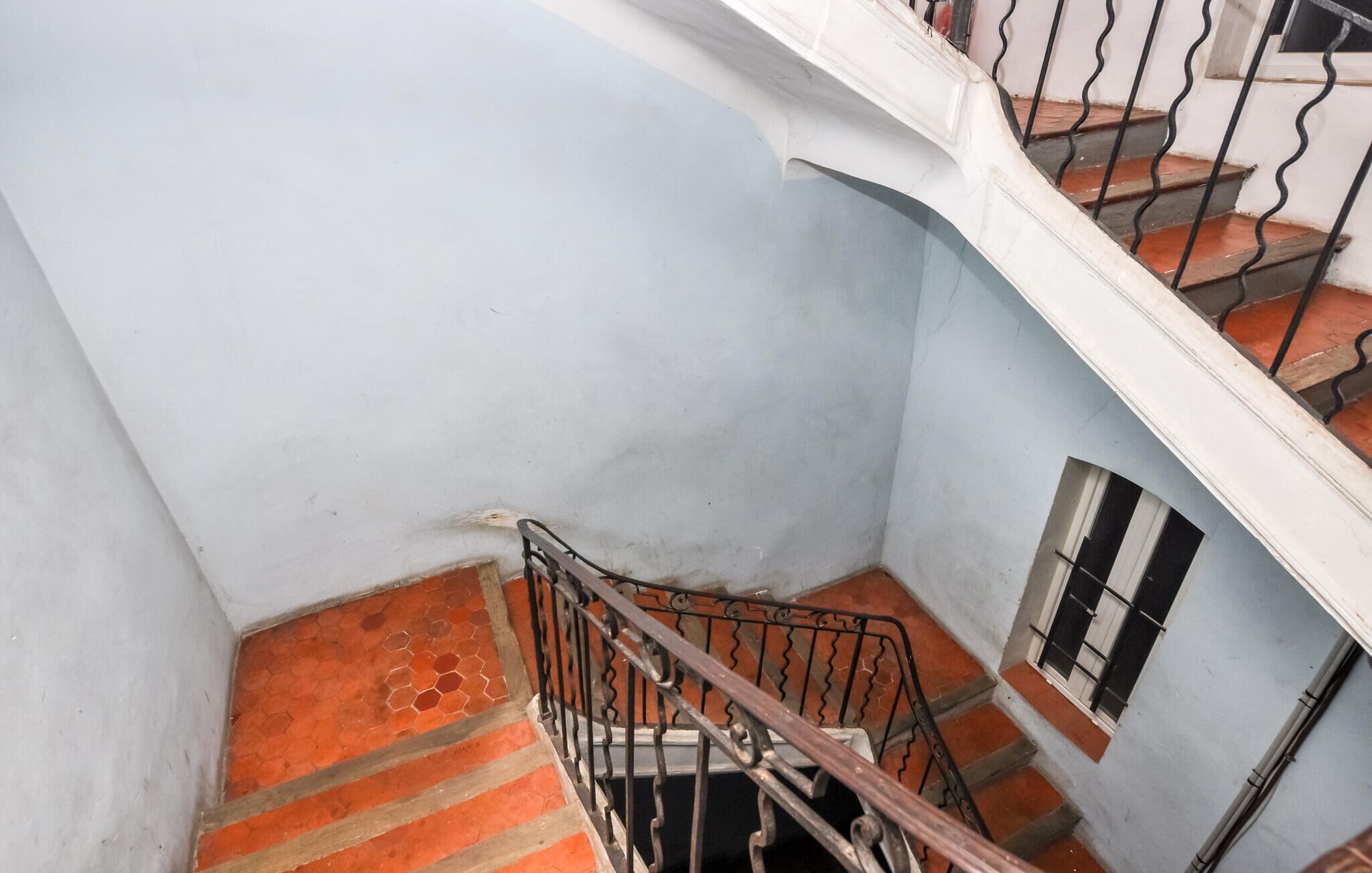 A staircase with a metal railing, a red-tiled floor, and a light blue wall.