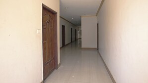 A long, narrow hallway with a wooden door on the left and a plain wall on the right. - JAYA BHARATHI LODGE (Vilavancode)