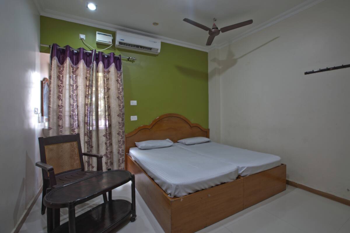 A bedroom with a bed, a chair, a ceiling fan, and an air conditioning unit.