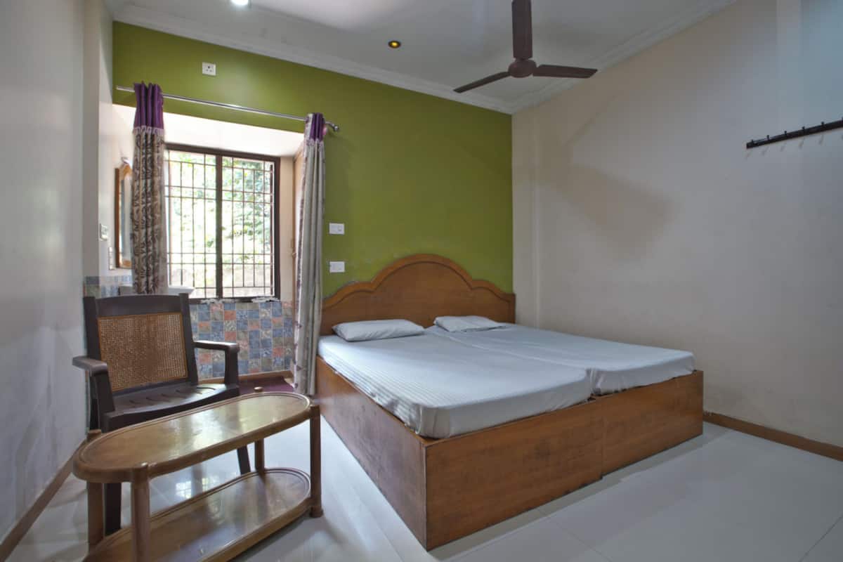 A bedroom with a bed, a chair, a table, and a window with curtains.