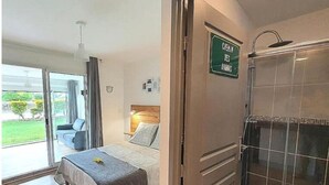 Un dormitorio con cama, mesita de noche, ventana y baño con ducha.
