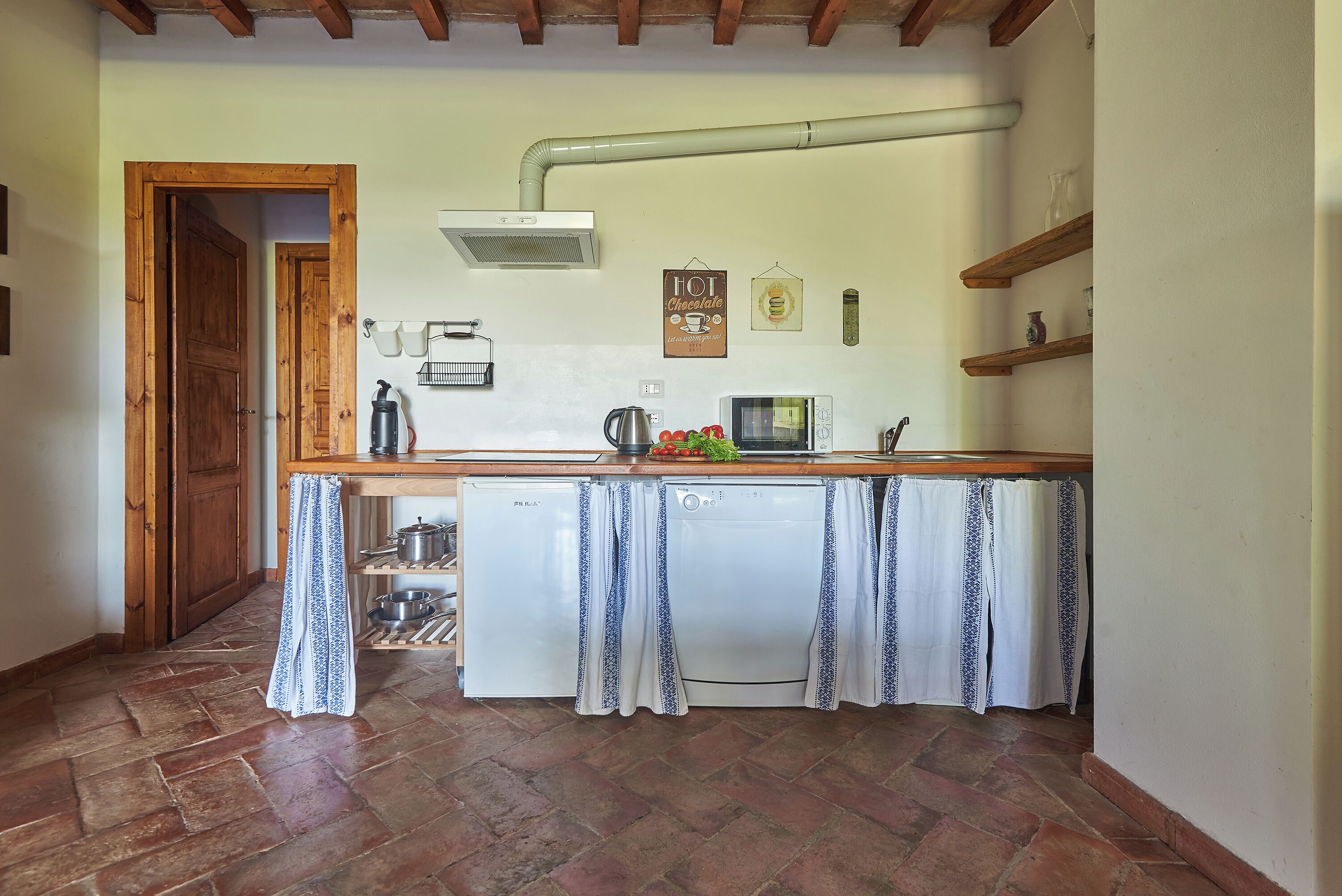 Cocina compacta con encimera de madera, lavavajillas blanco y un colgador para ollas.