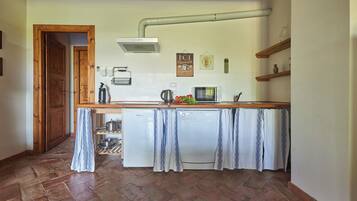 Cocina compacta con encimera de madera, lavavajillas blanco y un colgador para ollas.