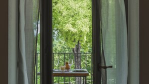 Una puerta abierta con vistas a un balcón, una mesa con un florero y un vaso, y un árbol afuera.