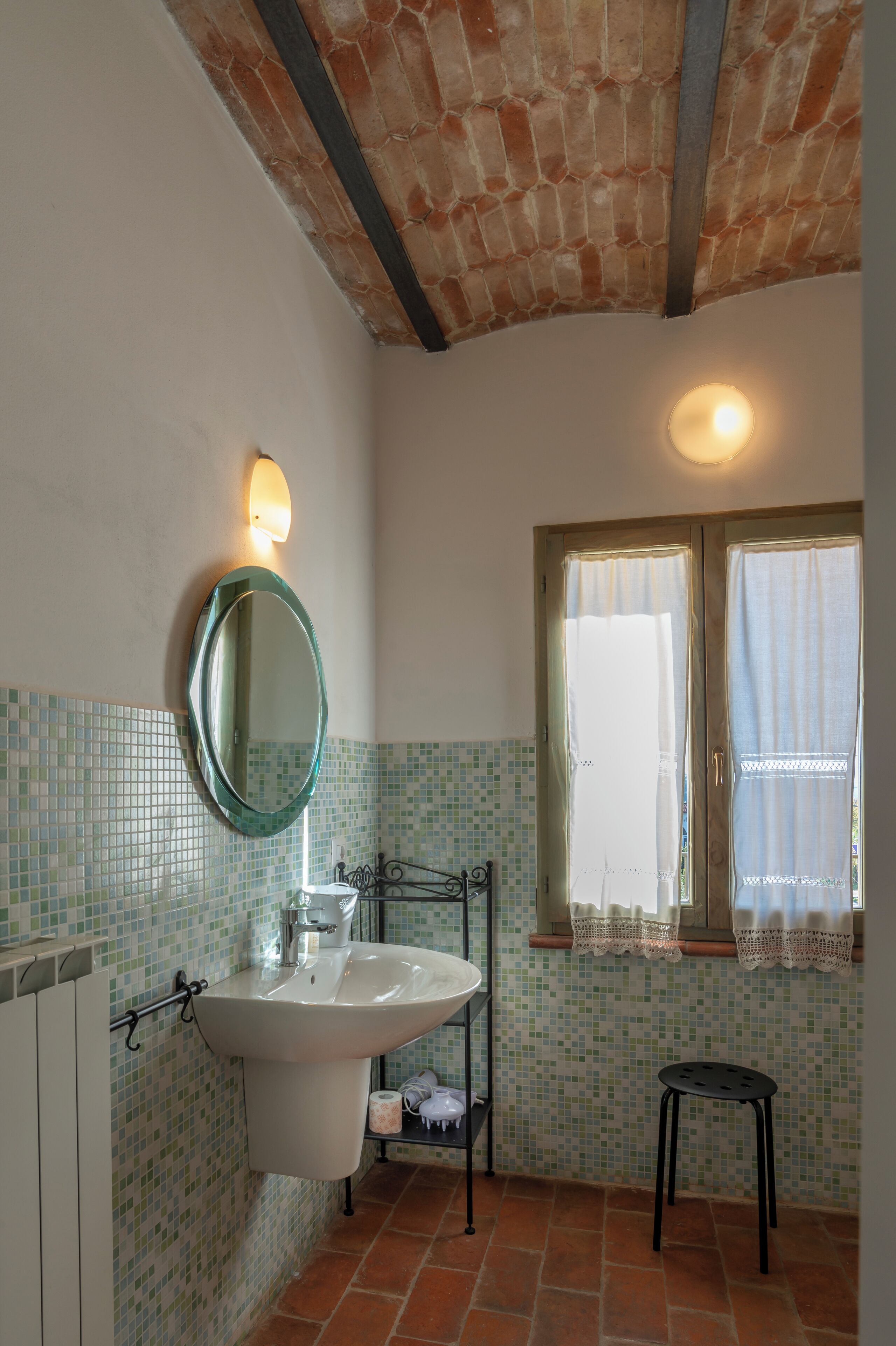 A bathroom with a tiled floor, a sink, a mirror, a window with curtains, and a radiator.