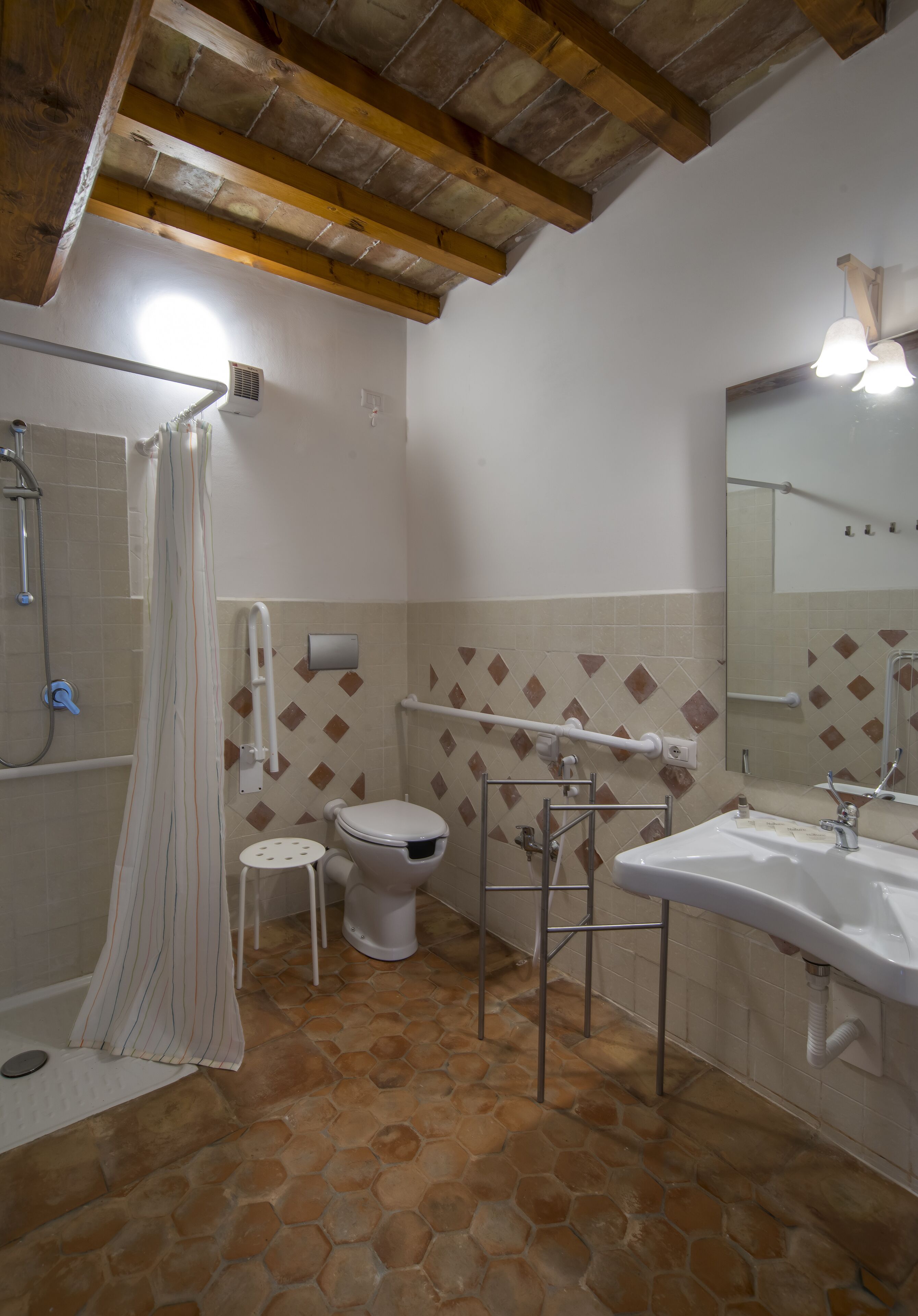 Une salle de bain équipée d’une douche, de toilettes et d’un lavabo, avec un sol carrelé et des poutres en bois au plafond.